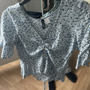 En blå t-shirt med vita blommor på - En blå t-shirt med vita blommor på, finns en stretch som man kan dra så det blir kortare. Skön material 