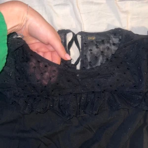 Svart topp från Maje - Säljer en superfin svart topp från Maje. Den har ett prickigt mönster och är dekorerad med volanger vid halsen. Perfekt för en festlig kväll eller en stilren vardagslook.