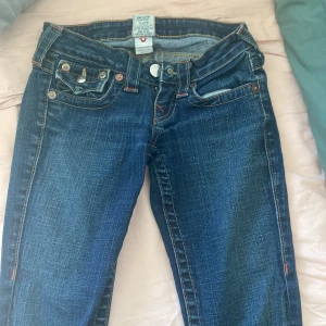 Jeans från True Religion - Säljer ett par snygga jeans från True Religion i mörkblå denim. De har en klassisk femficksdesign med coola detaljer som knappar och broderade, jag tycker att man känner sig så snygg när man har på sig dessa jeans 