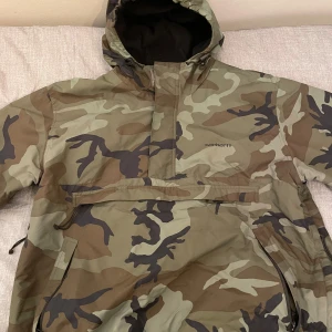 Camouflagejacka från Carhartt - snygg camouflagejacka från Carhartt. Den har en stor ficka framtill. Perfekt för höst och vår, och den är vattentät. Jackan är långärmad och i nyskick.