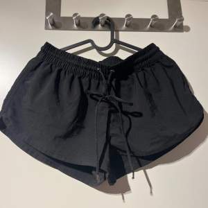 Säljer ett par svarta shorts med elastisk midja och knytband framtill. De är perfekta för en avslappnad dag eller träning. Materialet känns lätt och bekvämt, vilket gör dem idealiska för varma dagar.