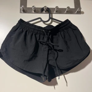 Svarta shorts med knytband - Säljer ett par svarta shorts med elastisk midja och knytband framtill. De är perfekta för en avslappnad dag eller träning. Materialet känns lätt och bekvämt, vilket gör dem idealiska för varma dagar.