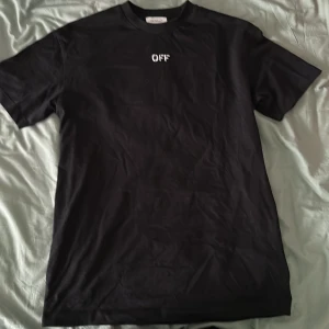 Svart t-shirt från Off-White - Säljer en svart t-shirt från Off-White med det ikoniska 'OFF' trycket på framsidan och ett stort grafiskt mönster på baksidan. T-shirten är i bomull och har en normal passform. Perfekt för en casual look!