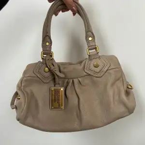 Säljer en superfin beige handväska från Marc Jacobs i skinn. Den har snygga gulddetaljer och dragkedja. Axelrem ingår 🤎