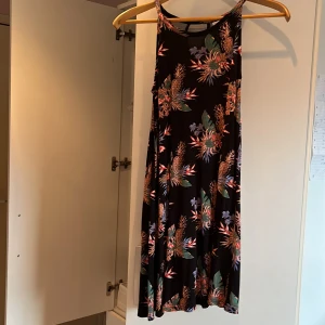 Blommig klänning från Lindex - Säljer en superfin blommig klänning från Lindex i storlek 146/152 för barn 10-12 år. Klänningen har ett färgglatt blommönster på en svart bakgrund och är ärmlös, perfekt för sommardagar. Den är i nyskick och från ett rök och djurfritt hem!