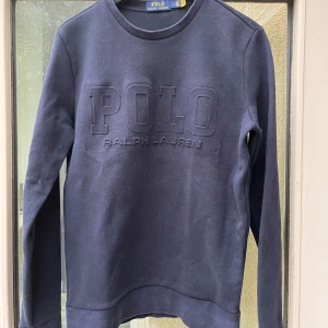 Mörkblå tröja från Ralph Lauren - Säljer en snygg mörkblå tröja från Ralph Lauren med POLO-logga i relief på framsidan. Tröjan är i bra skick och perfekt för både vardag och lite finare tillfällen. 