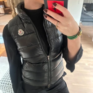Svart dunväst från Moncler - Säljer en snygg svart dunväst från Moncler. Västen är i mycket bra skick. Knappt använd. Storlek XS. Passar utmärkt att ha över tjocktröjor på kyligare dagar. Passform true to size. Bara att höra av er om ni vill ha mer information eller bilder 