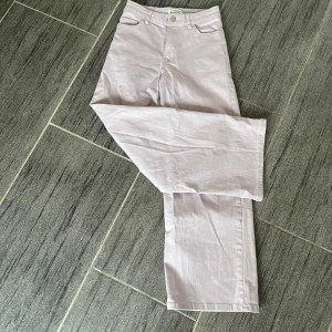 Ljuslila byxor från Lindex - Säljer ett par ljuslila byxor från Lindex i storlek 134. De har en hög midja och en rak, vid passform som ger en avslappnad stil. Byxorna är i mycket bra skick och gjorda av ett mjukt bomullsmaterial.