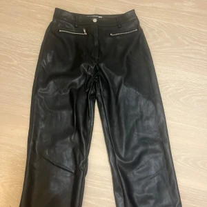 Svarta skinnbyxor från NA-KD - Snygga svarta skinnbyxor från NA-KD i storlek 36. Byxorna har en hög midja och dragkedjor som detaljer framtill. Perfekta för en cool och stilren look, passar både till vardags och fest. 🖤