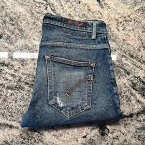 Blå jeans från Brighton - Säljer ett par snygga jeans från Dondup i storlek 31. De har fina slitningar på knäna och är av modellen Brighton. Perfekta för en avslappnad vardagslook. Passformen är normal och de är i bra skick.