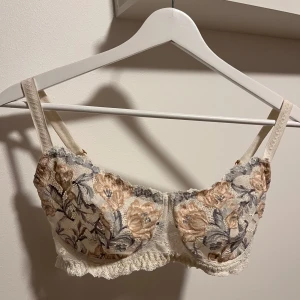 Blommig spets-BH från Intimissimi - Säljer en superfin BH från Intimissimi med blommigt mönster i beige och grått. Den är i spets och har justerbara axelband för perfekt passform. Perfekt för att känna sig extra fin till vardags eller speciella tillfällen. 🥰 väldigt lite använd! 