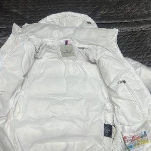 Moncler maya - Säljer en snygg vit dunjacka från Moncler i mycket bra skick. Jackan har en dragkedja framtill och en mysig huva för extra värme. Perfekt för kalla vinterdagar! Den är quiltad och har en stilren design som passar till det mesta. 👍