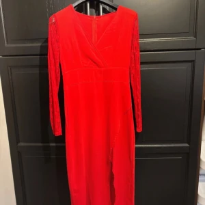 Röd långklänning med spetsdetaljer - Säljer en elegant röd långklänning med v-ringad design och långa spetsärmar. Perfekt för festliga tillfällen. Klänningen har en dragkedja i ryggen för enkel påklädning. Materialet är mjukt och bekvämt, vilket gör den idealisk för både höst och vinter.