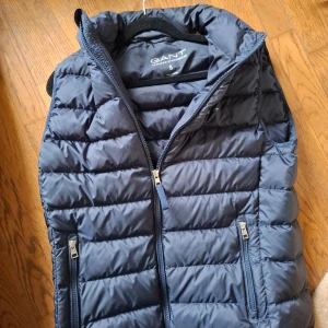 Mörkblå dunväst från GANT - Säljer en galet snygg och varm mörkblå dunväst från GANT i storlek S. (Passar m). Perfekt för kyliga höstdagar eller som ett extra lager under vintern. Västen är i mycket bra skick och redo för nya äventyr! Skick 10-10 skriv om ni har några fu drinkar priset kan absolut diskuteras mvh simon🤗🤗