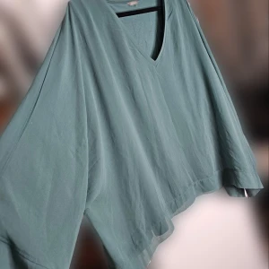 Grön/turkos v-ringad topp - Säljer en luftig grön topp med v-ringning i storlek XL. Den är tillverkad i 100% polyester med ett foder av lyocell och viskos. Den har vida ärmar i mesh men på överkroppen är det en undertröja. Väldigt stilren topp.