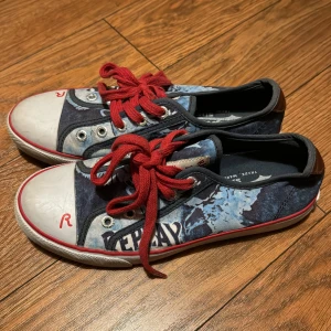 Snygga sneakers från Replay - Coola sneakers från Replay med en unik design och örnmotiv. De har en blå denimlook med röda snören och detaljer. Skorna har en vit tåhätta med ett rött 'R' och Replay-loggan på hälen. Storlek 36. 🦅✨