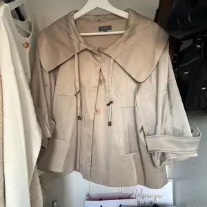 Säljer en superfin beige trendig kappa från Sisley. Den har en stor krage och knappar framtill. Ärmarna är trekvarts och det finns snörning vid kragen. Perfekt för vår och höst! Köpt på Vinted för 400 kr