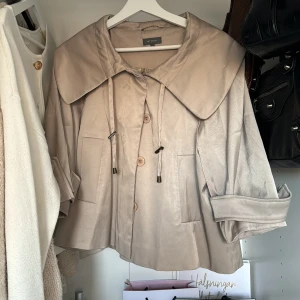 Beige trekvarts kappa från Sisley - Säljer en superfin beige trendig kappa från Sisley. Den har en stor krage och knappar framtill. Ärmarna är trekvarts och det finns snörning vid kragen. Perfekt för vår och höst! Köpt på Vinted för 400 kr