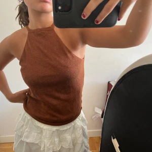 Brun oneshoulder topp - Säljer en snygg brun/koppar topp. Den är tight och ärmlös, perfekt för sommaren eller en festkväll. Toppen är gjord av ett mjukt och bekvämt material som sitter skönt på kroppen. Passar bra till både kjol och byxor!