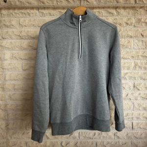 Grå tröja från Oscar Jacobson - Säljer en snygg och stilren grå tröja från Oscar Jacobson. Tröjan har en dragkedja framtill och en hög krage som ger en sportig look. Den är långärmad och tillverkad i ett mjukt och bekvämt material, perfekt för både vardag och träning. Tröjan är i nyskick och har en normal passform.