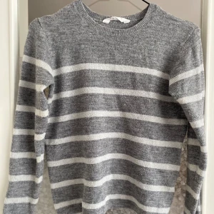 Grå och vit randig stickad tröja - Säljer en superfin grå och vit randig stickad tröja. Den är i storlek S och har långa ärmar. Perfekt för höst och vinter, den är både varm och stilren. Tröjan är i nyskick och passar perfekt till både vardag och fest. 🧶✨