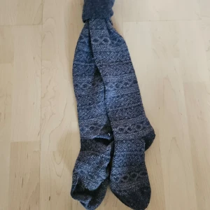 Mönstrade grå knästrumpor - Säljer ett par snygga och bekväma grå strumpor med ett diskret mönster. Perfekta för att hålla fötterna varma under vintern. Strumporna är i nyskick och redo att användas. 100% ull