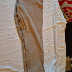 Beige byxor från Soyaconcept - Säljer ett par snygga beige byxor från Soyaconcept i storlek 44. Byxorna har en klassisk design med dragkedja och knappar framtill. Perfekta för både vardag och lite mer uppklädda tillfällen. De är i bra skick och väldigt bekväma att ha på sig.