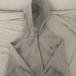 Grå hoodie från Polo Ralph Lauren - Säljer en snygg och bekväm grå hoodie från Polo Ralph Lauren. Den har en dragkedja framtill och en liten broderad logga på bröstet. Perfekt för höst och vinter, och passar både till vardags och avslappnade tillfällen. Hoodien är i bra skick och väldigt mysig att ha på sig. Köp direkt eller ge prisförslag! 💛