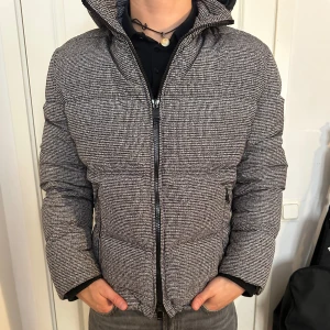 Ny Vinter Dunjacka Från Hugo Boss - Säljer en snygg rutig dunjacka från Hugo Boss i storlek M. Jackan är i  helt nytt skick! Även fylld med 80% ankdun och 20% ankfjädrar, vilket gör den riktigt varm och skön. Den har en dubbelsidig dragkedja och en huva för extra skydd mot kyla. Perfekt för vintern! Modellen är 182 cm och väger 75 kg. Pris går att diskuteras!