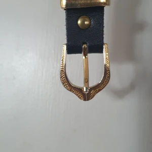 Svart skärp med guldfärgat spänne - Säljer ett snyggt svart skärp med ett guldfärgat spänne. Skärpet är gjort av skinn och har en klassisk design som passar till många olika outfits. Perfekt för både vardag och fest!