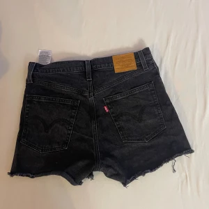 Svarta jeansshorts från Levi's - Säljer ett par svarta jeansshorts från Levi's i storlek XS. De är högmidjade och har en knappgylf. Shortsen har en rå kant nertill som ger en cool och avslappnad look. Perfekta för sommaren!