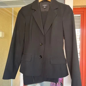Svart kostym från Mexx - Säljer en elegant svart kostym från Mexx i storlek 32. Kostymen består av en kavaj med två knappar och byxor. Kavajen har en klassisk design med fickor och en smickrande passform. Perfekt för formella tillfällen eller kontorsbruk. Byxorna är en rak modell med två fickor fram och en bak. Kostymen är i mycket bra skick och redo att användas.