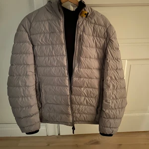 Beige quiltad jacka från Parajumpers - Säljer en snygg grå quiltad jacka från Parajumpers. Den har en dragkedja framtill och är långärmad. Perfekt för höst och vår när du vill hålla dig varm men ändå se stilren ut. Jackan har en huva och är i nyskick. Passar perfekt för både vardag och f