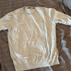 Gant tröja  -  En grå Gant tröja  i bomullsmix riktigt sköna ha på sig och man kan styla en snyggt med att ta en skjorta under inget tecken på användning och skicket är som nytt med inga defekter