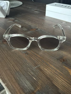 Gråa transparenta 02 glasögon från chimi  - Snygga solglasögon med transparent plastbåge och runda linser. Glasen är lätt tonade och ger en cool, modern vibe. Perfekta för dig som vill sticka ut med en stilren accessoar. 
