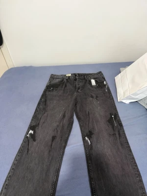 Svarta jeans med tryck från Off-White - Säljer ett par svarta raka jeans från Off-White med unikt vitt tryck på bakfickan och färgstänk-detaljer. Jeansen har fem fickor, bälteshällor och klassisk knappgylf. Perfekta för dig som gillar streetwear och vill sticka ut. Helt nya jeans, köpta för 1700 kr 