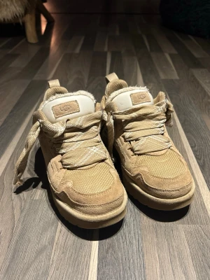 Ugg Lowmel i färgen Sand - Snygga beige sneakers från UGG med bred snörning i mycket bra skick! Ovandelen är i mocka och textil, och insidan är fodrad med mjuk päls för extra komfort. Perfekta för dig som inte vill frysa! Kontakta vid frågor! Priset är prutbart vid snabb affär!!(OBS!! Bra att ha i en strl större, dessa är perfekta om du vanligtvis har strl 39)