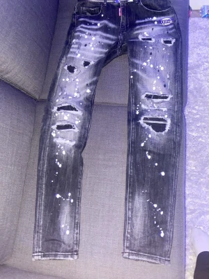 Dsquared2 jeans - Säljer ett par svarta jeans med slitningar och vita färgstänk över hela byxorna. Köpta i Italien på sommaren men har växt ur dem nu har påsen kvar tror jag kan skicka med om den hittas!