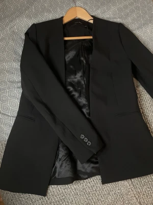 Svart kavaj från Zara Basic Collection - Svart kavaj från Zara Basic Collection i klassisk modell. Kavajen har två fickor fram och knappar vid ärmslut. 