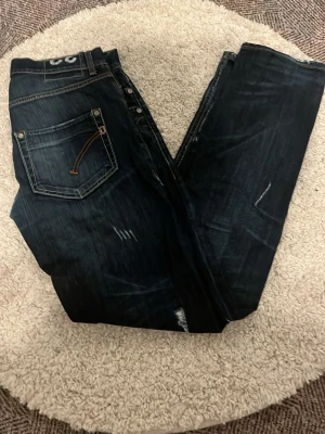 Mörkblå Dondup jeans straight fit - Säljer ett par mörkblå jeans från Dondup med snygga slitningar och kontrastsömmar. Modellen har raka ben och klassiska fem fickor. Jeansen är tillverkade i slitstarkt denim och har coola detaljer på bakfickorna.