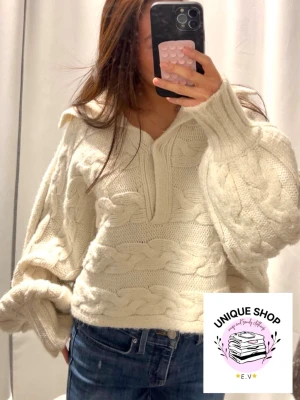 Bejge unik kabelstickad tröja med knapp - Säljer en chunky vit kabelstickad tröja med  knapp och krage. Töjan har oversized passform, kortare modell och  ballongärmar och är gjord i mjukt, tjockt material. Perfekt för dig som gillar en avslappnad och trendig look.