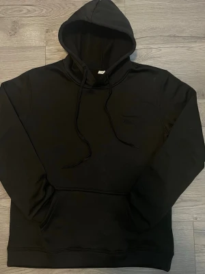 Svart hoodie med magficka och huva - En stilren svart hoodie i 100 % polyester med mjuk och skön känsla. Medium-passform som sitter bekvämt och passar perfekt till vardag och fritid. Lättskött, hållbar och alltid rätt i stil.