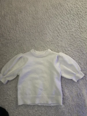 Vit puffärm stickad tröja Gina Tricot - Supersöt vit stickad tröja från Gina Tricot med trendiga puffärmar och ribbade muddar vid hals, ärmslut och nederkant. Perfekt för dig som gillar en enkel men ändå stylish look. Materialet känns mjukt och bekvämt mot huden.