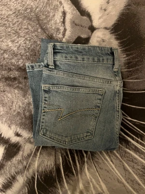 Blå bootcut jeans med broderad ficka - Snygga ljusblå bootcut jeans med en unik broderad detalj på bakfickan. Klassisk femficksmodell i mjuk bomullsdenim. Perfekta för dig som gillar en avslappnad men trendig look. I storlek xs