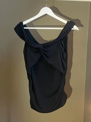 Svart offshoulder topp med twist - Snygg svart offshoulder topp med twistad detalj framtill. Toppen har en elegant drapering och ärmlös design som ger en trendig look. Perfekt att styla med jeans eller kjol för en cool outfit. Köpt från Bik Bok, aldrig använt 🖤