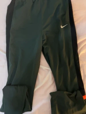 Mörkgröna mjukisbyxor från Nike XL - Mörkgröna mjukisbyxor från Nike med svarta sidor och vit logga på låret. Byxorna har resår i midjan och är perfekta för chill eller träning. Sköna och stilrena med klassisk Nike-look. Är sällsynta finns inte att köpa längre