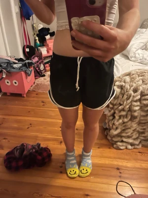 Svarta träningsshorts från Varsity Spirit - Svarta träningsshorts från Varsity Spirit med vita detaljer och snörning i midjan. Shortsen har en sportig look med elastisk midja och är perfekta för aktiva dagar. Lätta och bekväma, tillverkade i syntetmaterial.