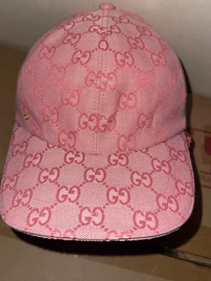  Gucc* keps  - Säljer en rosa keps från Gucc* med det klassiska G monogrammet över hela kepsen. Kepsen har böjd skärm och är tillverkad i ett slitstarkt tygmaterial. Perfekt för dig som vill sticka ut med en lyxig och trendig accessoar.