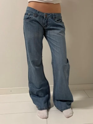 Blå bootcut jeans  - Säljer ett par ljusblå bootcut jeans med låg midja. Jeansen har klassisk femficksdesign, snygga slitningar på bakfickorna och raka, vida ben.  Midjemåttet 38 Innerbensländ 80 Grenmått 17