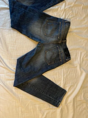 Armani junior blå jeans med raka ben (154cm) - Snygga blå jeans från Armani med klassisk femficksdesign och raka ben. Jeansen har en något tvättad look med ljusare partier och tydliga sömmar. Perfekta för en avslappnad stil och tillverkade i slitstarkt denimtyg.